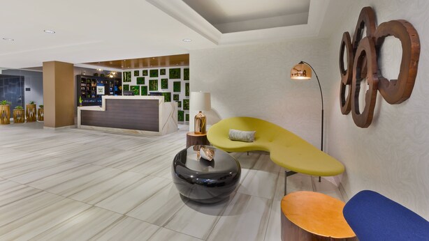 Een moderne lobby met een receptiebalie, een groene bank en een ronde, zwarte tafel.