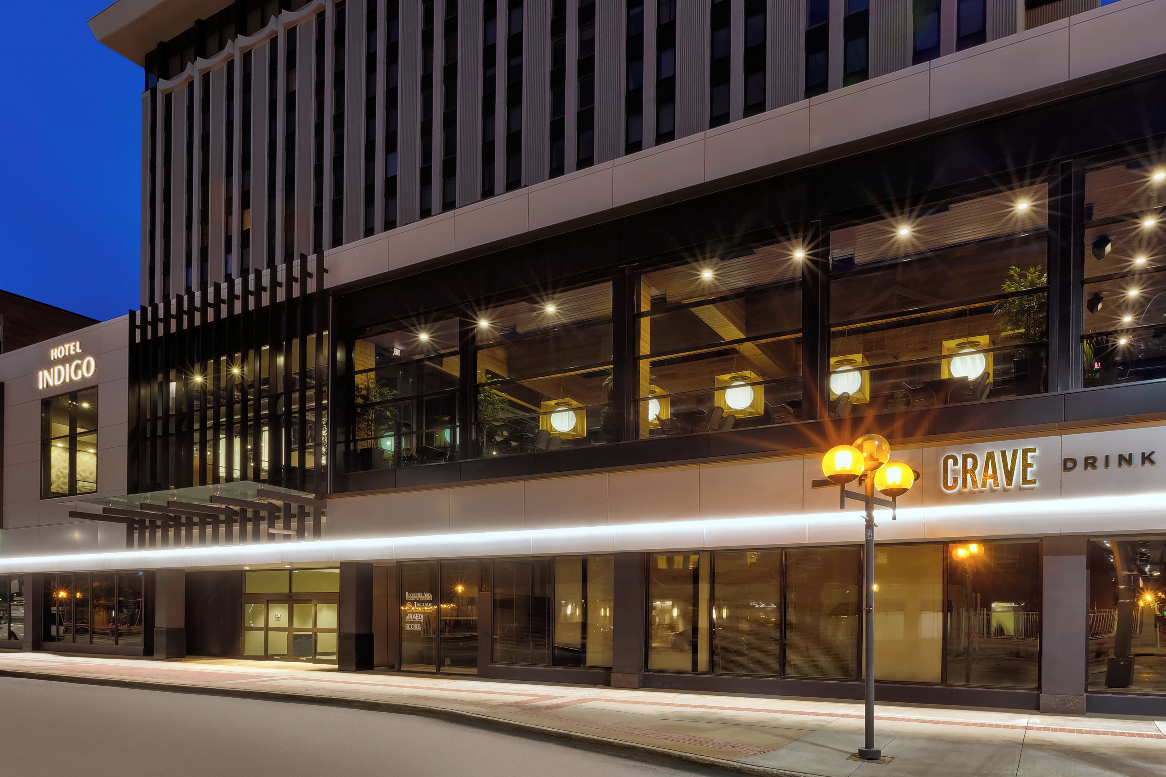 En modern hotellbyggnad med en tydlig skylt som visar namnet ”Hotel Indigo” och en bar/servering som heter ”Crave Drink”.