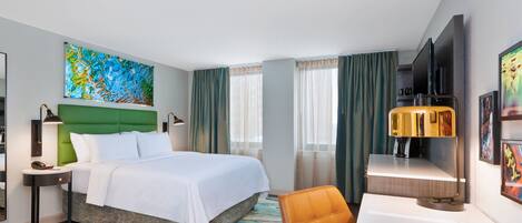 A hotel room with a large bed, a desk with a lamp, a television, and artwork on the walls.