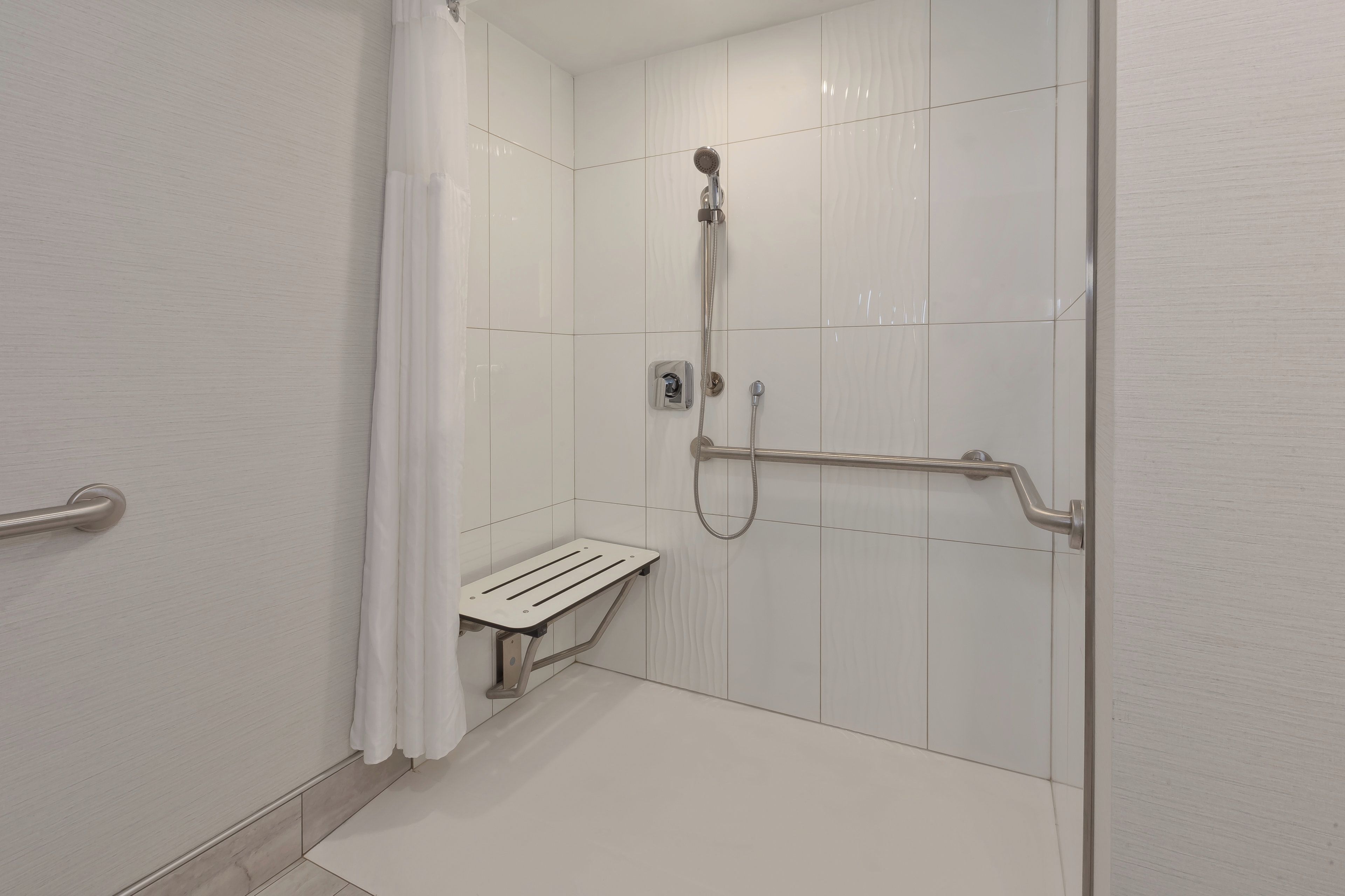 A modern shower area with a handheld showerhead, a handheld shower attachment, and a grab bar for support.