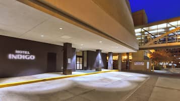 Entrada de hotel con diseño moderno, un letrero que dice 'Hotel Indigo' y una rampa que conduce al estacionamiento.