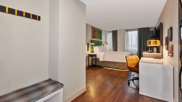 A hotel room with a bed, a desk, a chair, a sofa, and a TV.