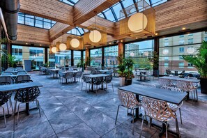 A spacious outdoor dining area with multiple tables and chairs, large windows, and a wooden ceiling structure. - Hotel Indigo Rochester – Mayo Clinic Area by IHG (Rochester)