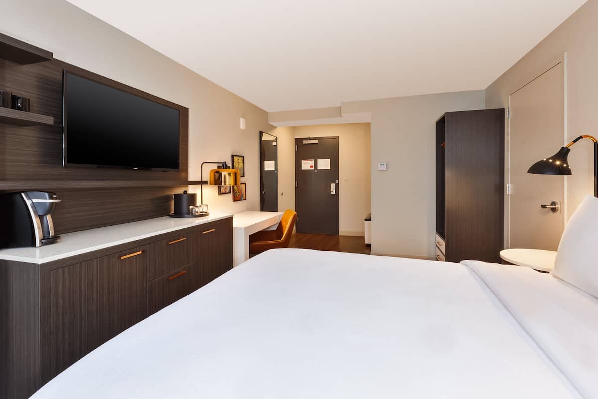 Une chambre d’hôtel moderne dotée d’un grand lit, d’un téléviseur à écran plat fixé au mur, d’un bureau avec une chaise et d’une table de chevet avec une lampe.