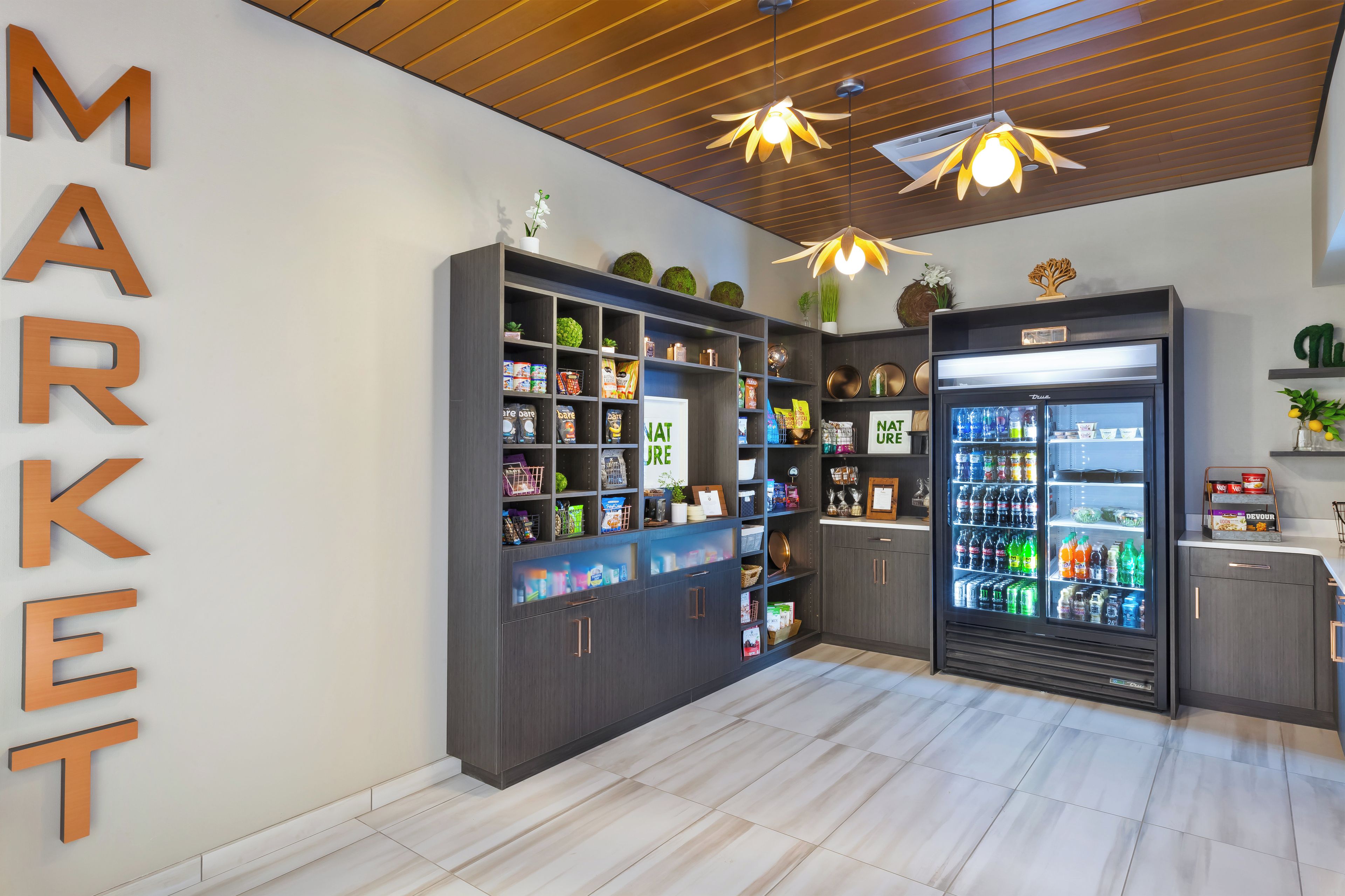 Een modern interieur met een houten plafond, een grote koelkast vol drankjes en planken met diverse producten.