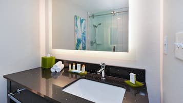 Un baño moderno con un espejo grande, encimera negra, lavamanos blanco y cabina de ducha de cristal.