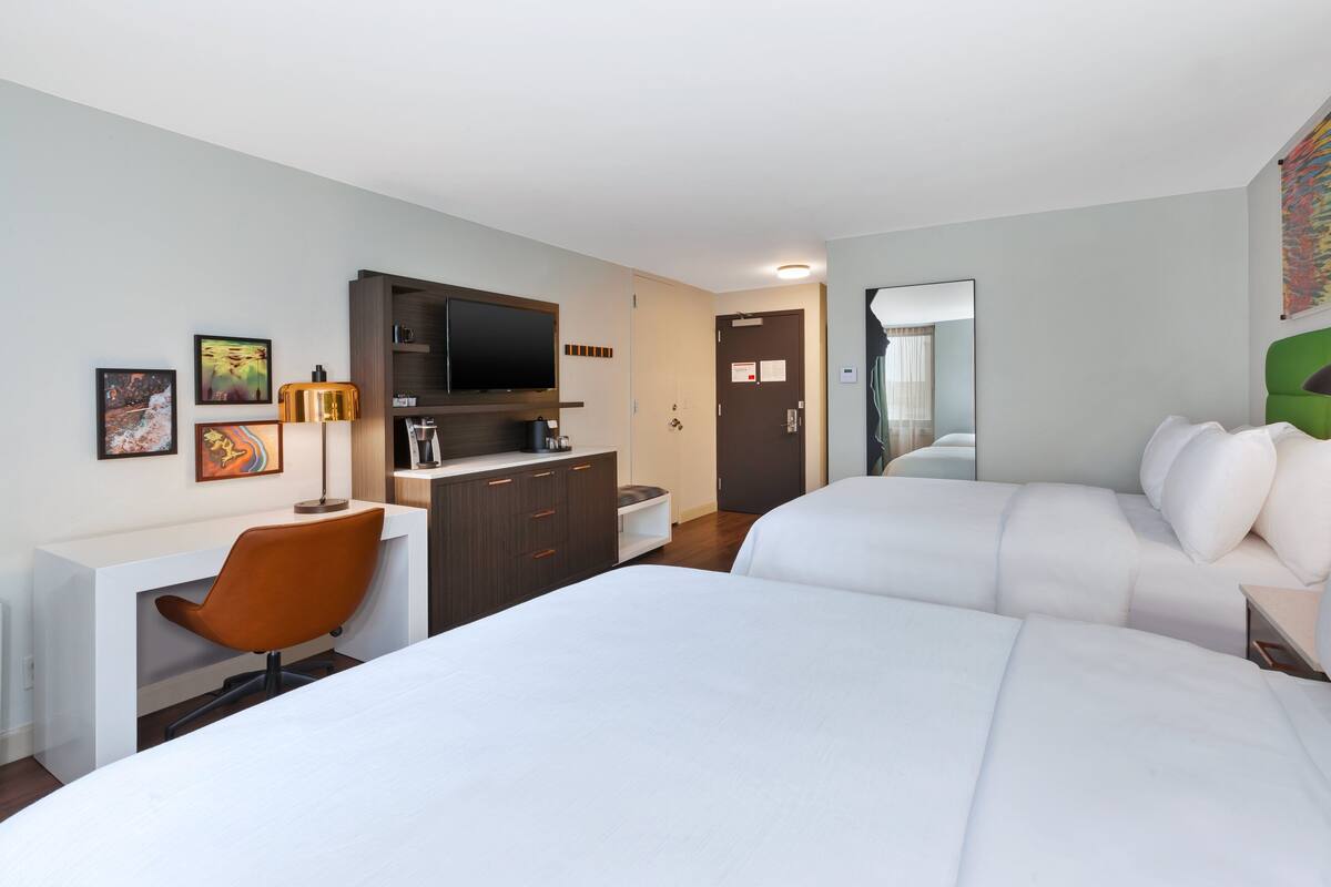 Une chambre d’hôtel avec deux lits, un bureau avec une chaise, une télévision et des œuvres d’art accrochées aux murs.