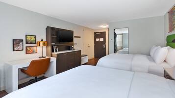 Ein Hotelzimmer mit zwei Betten, einem Schreibtisch mit Stuhl, einem Fernseher und Bildern an den Wänden.