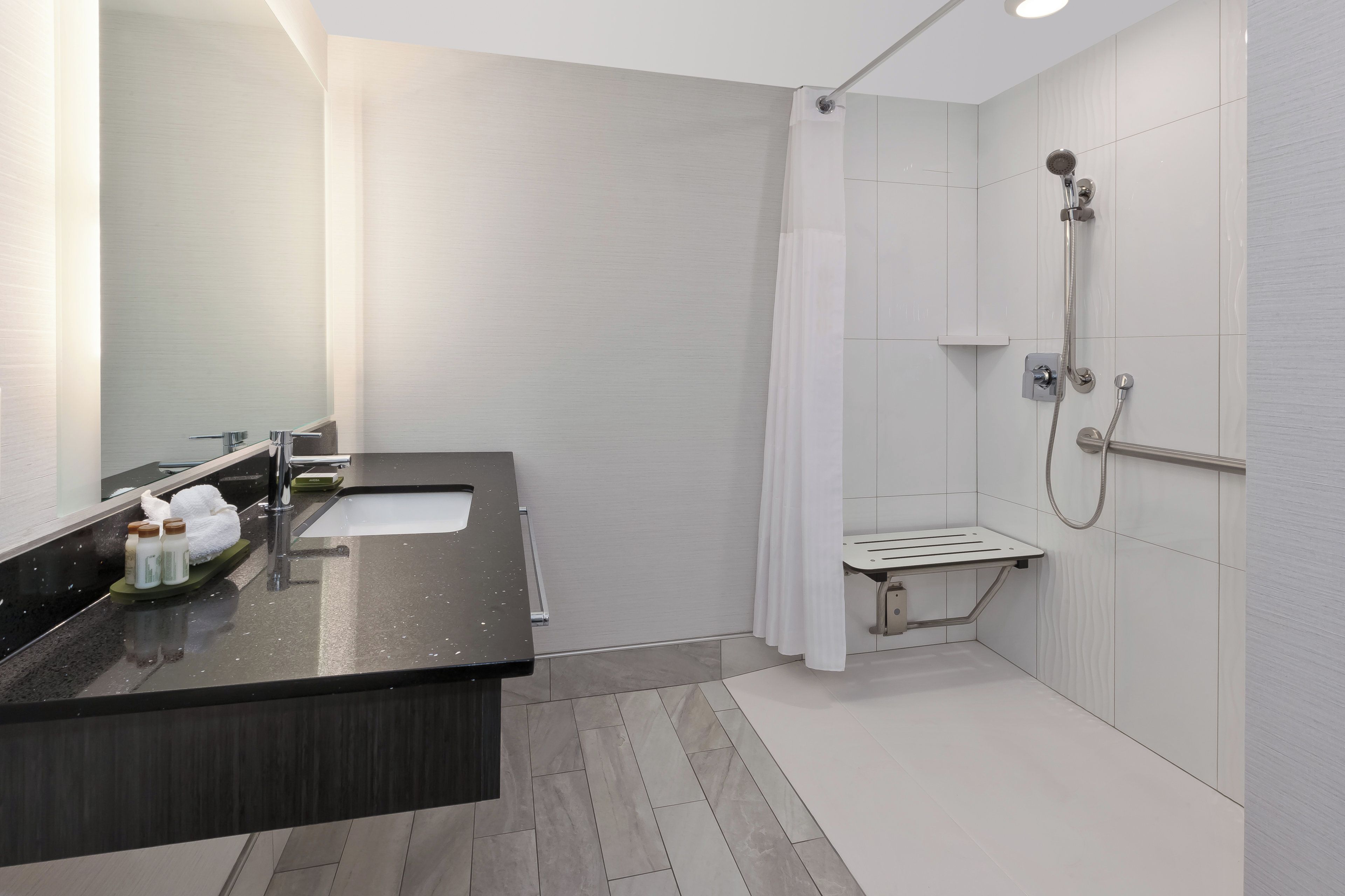 A modern bathroom with a dark countertop sink, a mirror, and a shower area with a handheld showerhead.