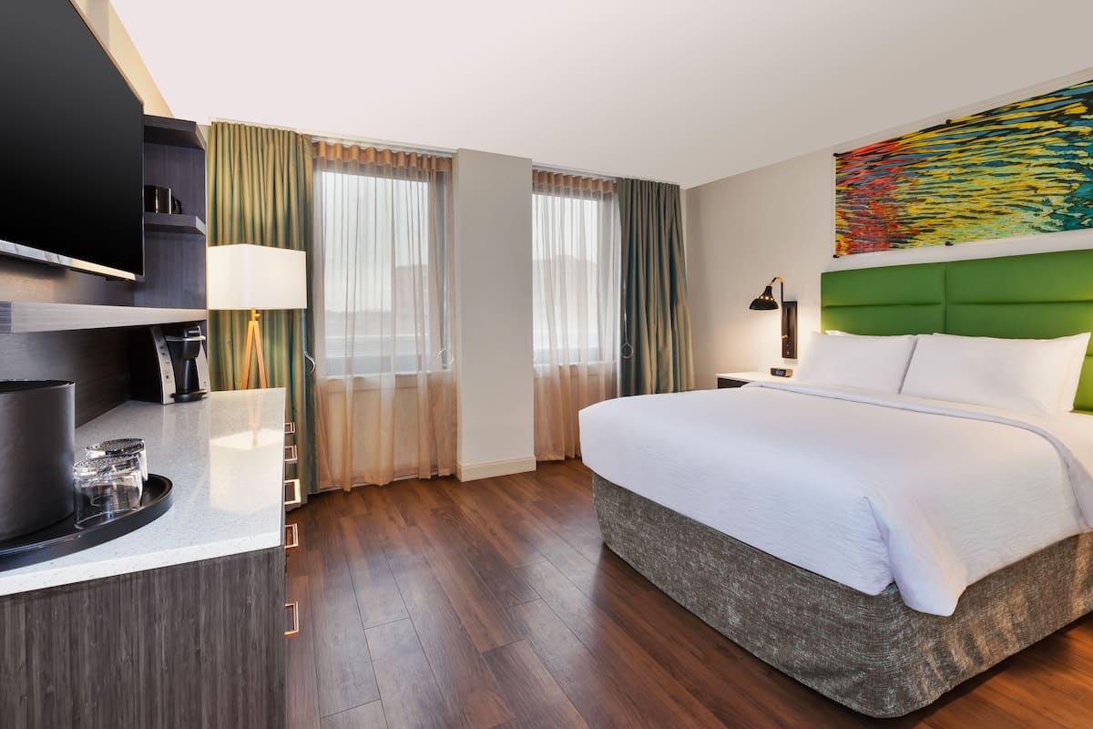 Une chambre d’hôtel avec un grand lit, un téléviseur à écran plat, un bureau avec une lampe et une fenêtre avec des rideaux.