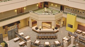 Monitasoinen hotellin aula, jossa on keskeinen oleskelualue, useita ruokapöytiä ja koristeellinen suihkulähde.
