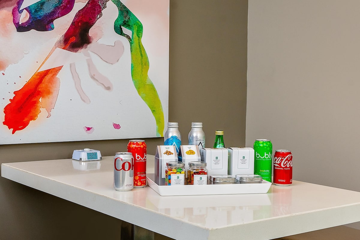 Une table blanche sur laquelle se trouvent différentes canettes et bouteilles de boissons, une horloge numérique et un plateau blanc avec des pots.