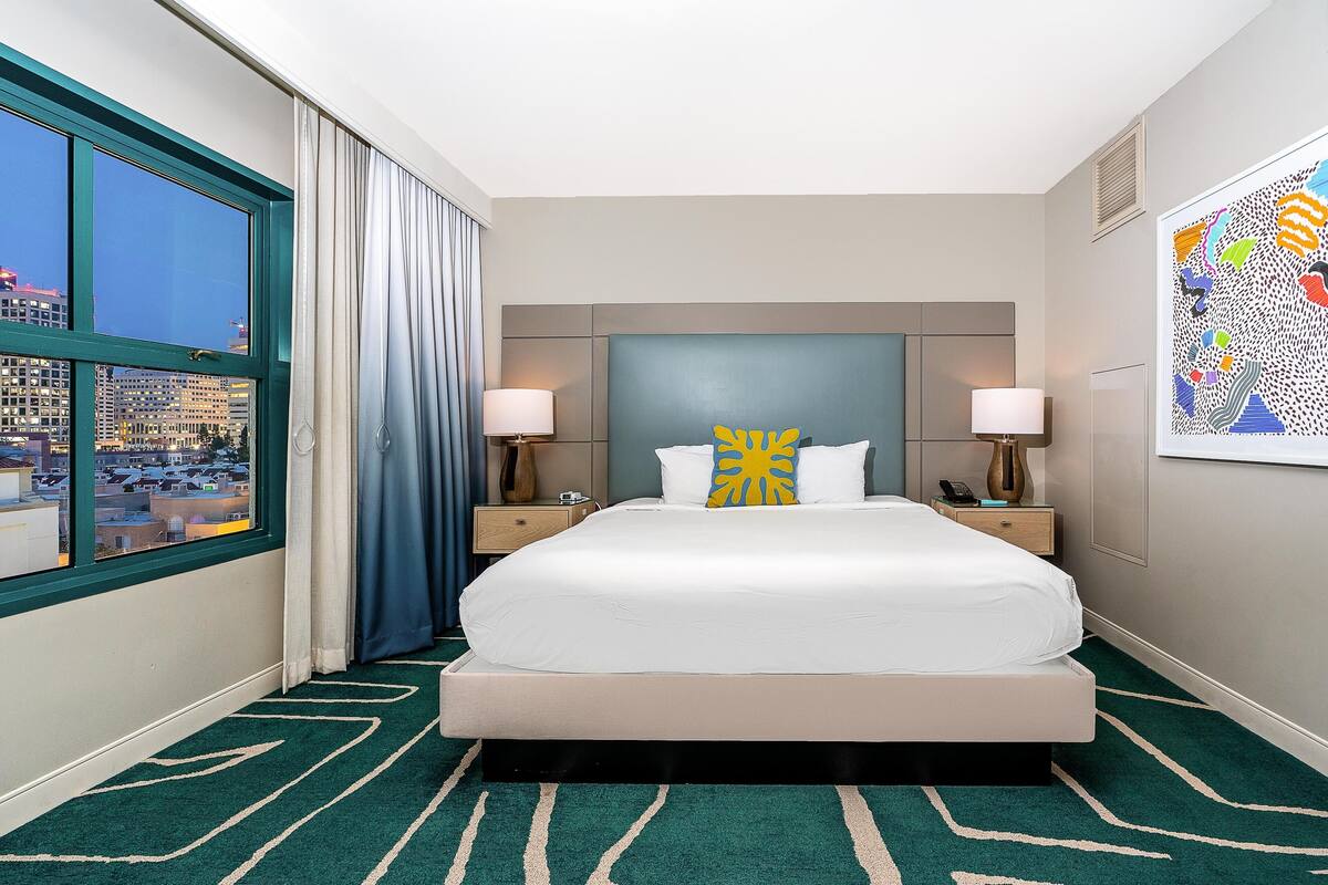 Une chambre d’hôtel avec un grand lit, deux tables de chevet, une fenêtre avec des rideaux et une vue sur la ville.