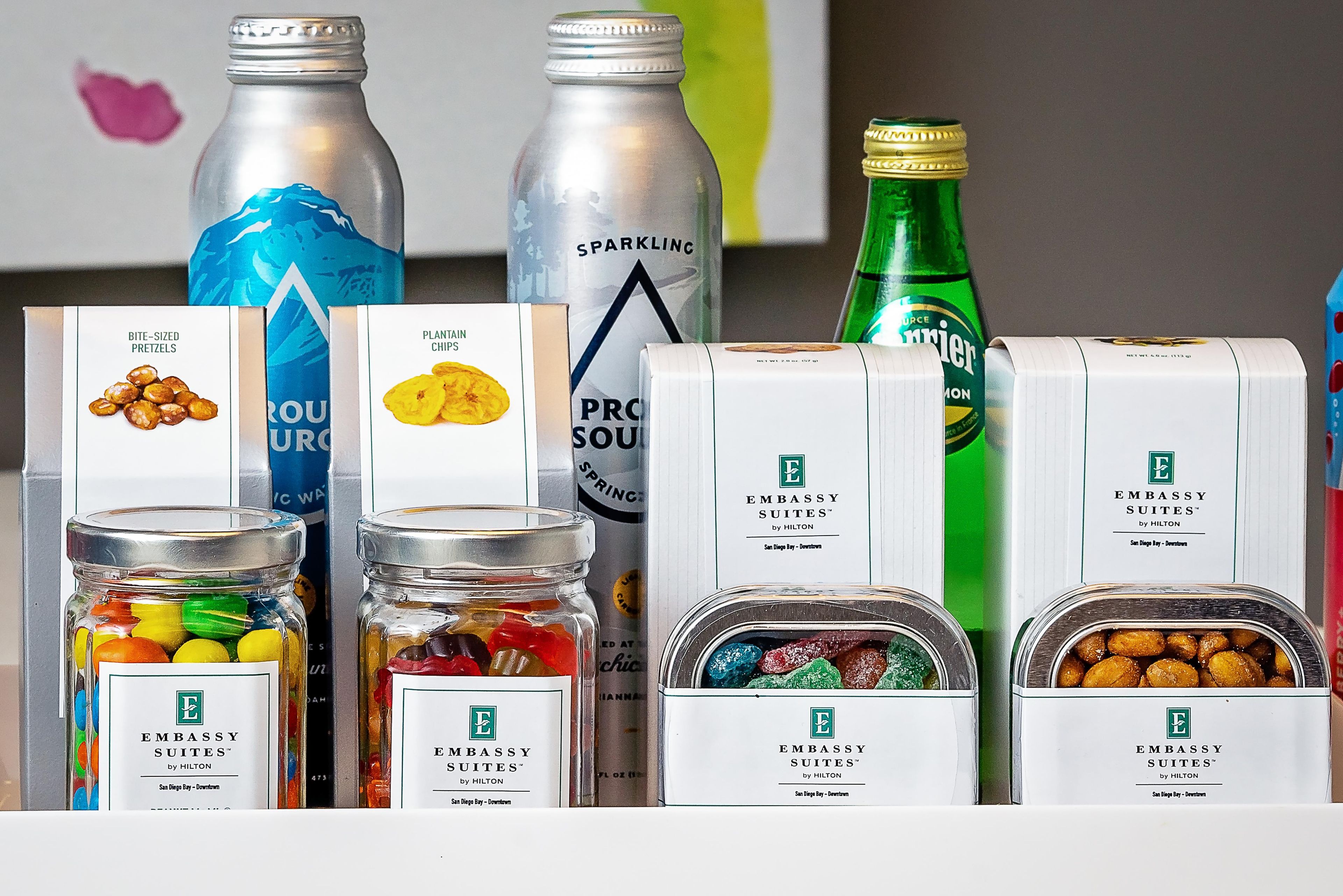 Una variedad de comida y bebidas, incluyendo pretzels en porciones pequeñas, chips de plátano y diversas opciones.