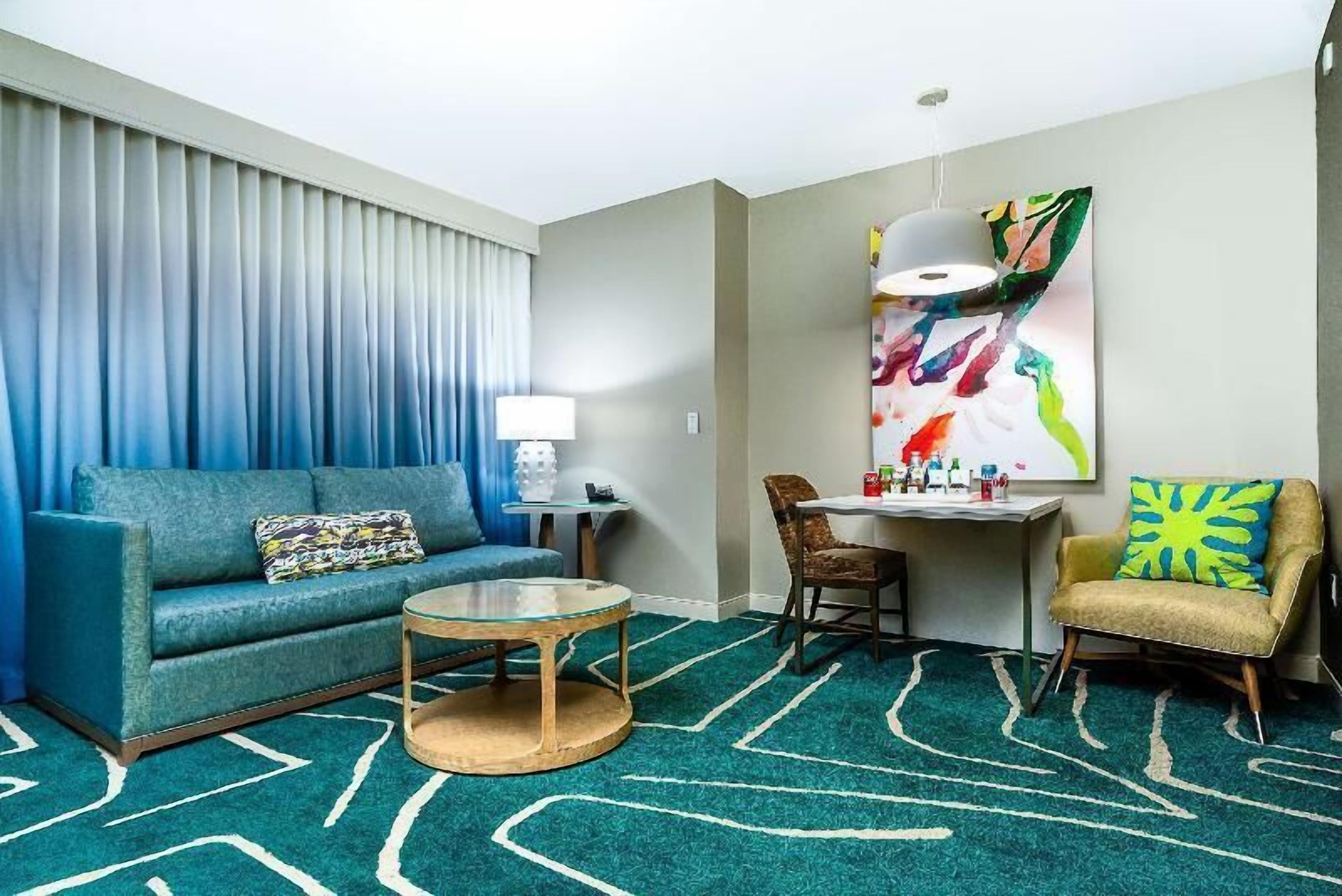 A hotel room with a sofa, armchair, round coffee table, and a painting on the wall.