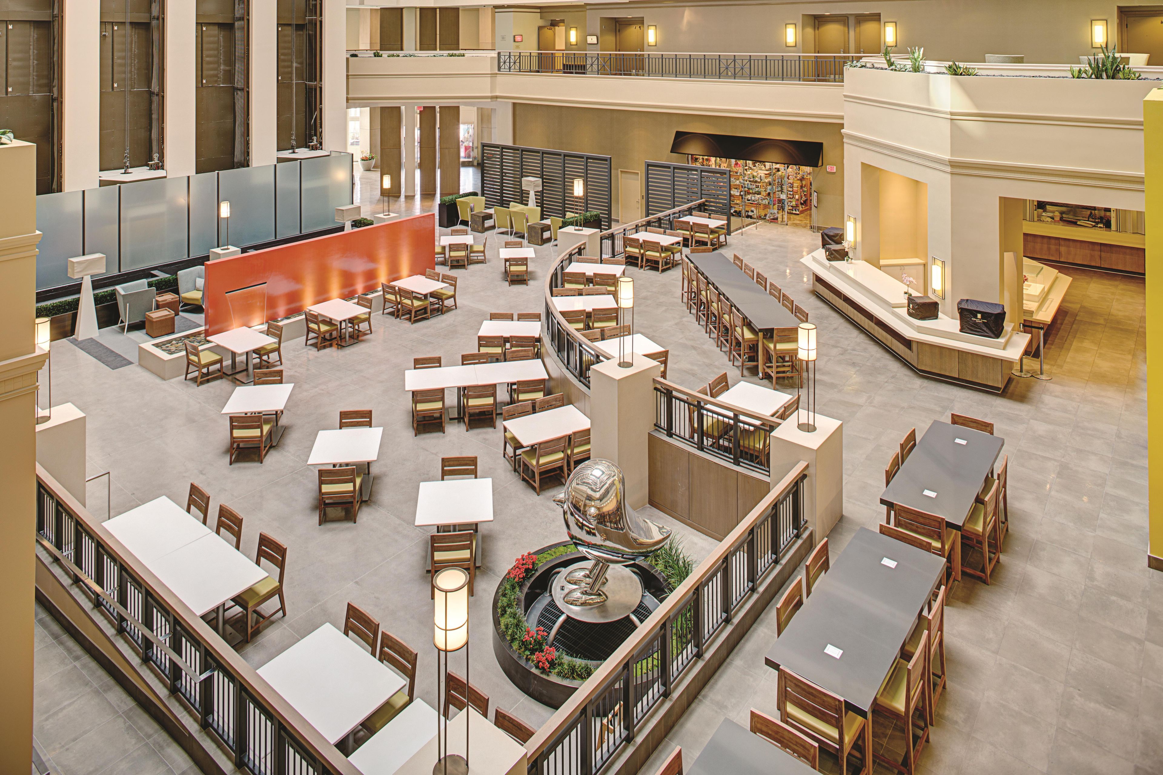 A spacious indoor area with multiple dining tables and chairs, a central decorative fountain, and a second-floor balcony with a railing.