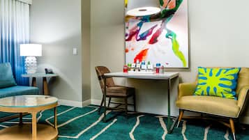 A hotel room with a sofa, armchair, small table, and a painting on the wall.