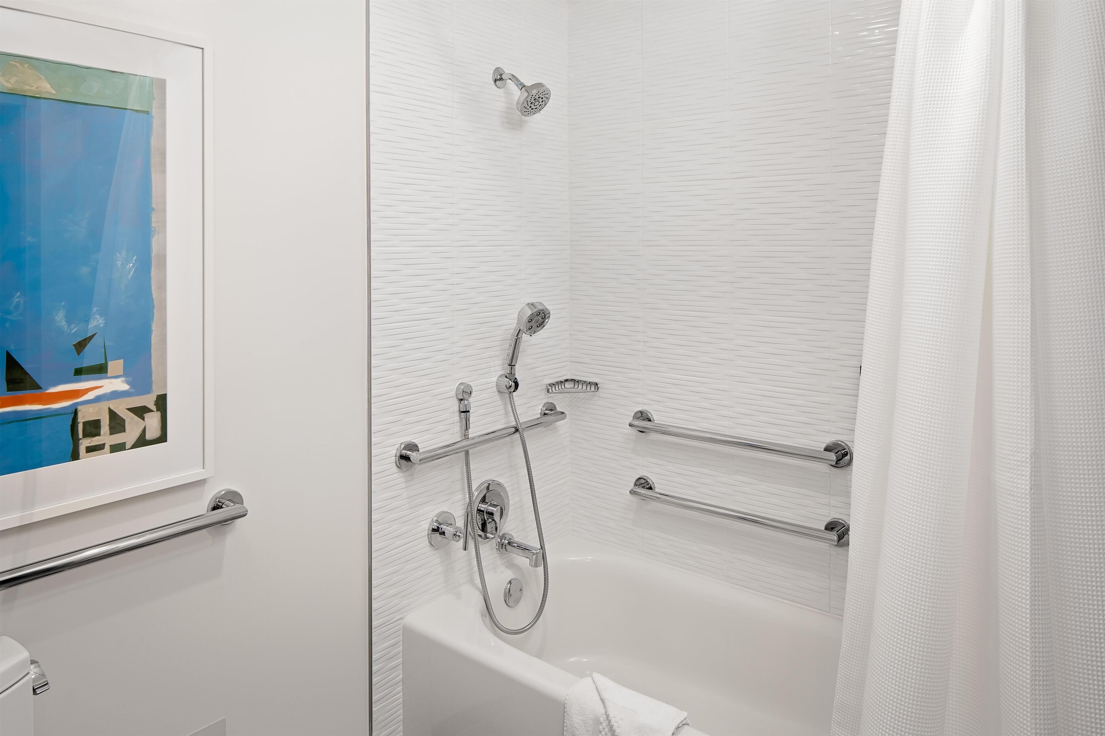 A modern bathroom with a bathtub, shower, and handrails.
