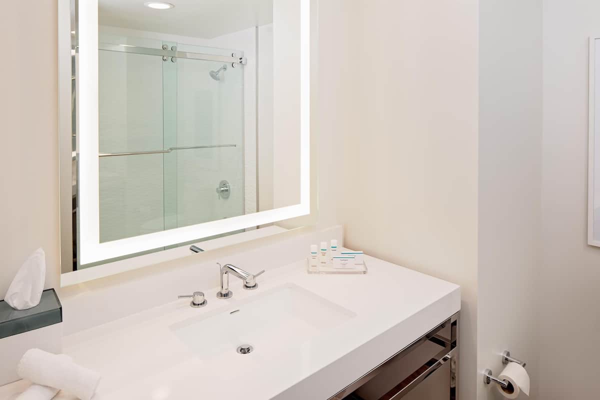 Une salle de bain avec un grand miroir, un lavabo blanc, une douche en verre et un porte-serviettes.