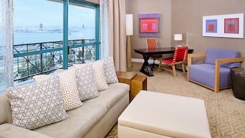 A hotel room with a sofa, a dining table, a chair, and a view of the water.
