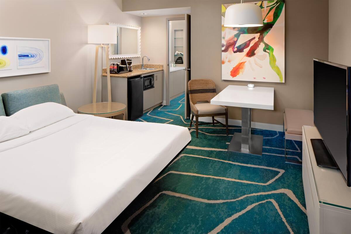 Une chambre d’hôtel équipée d’un lit, d’un bureau, d’une chaise, d’une télévision, d’un four à micro-ondes et d’une petite kitchenette.