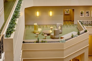 Un vestíbulo de hotel con una zona de estar, una escalera y vistas al vestíbulo.