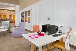 Een moderne kantoorruimte met een wit bureau, computer en printer, omringd door stoelen en een muur met kleurrijke kunstwerken.