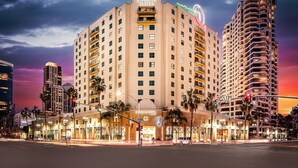 A multi-story building with 'Embassy Suites' signage, a prominent entrance, and a street view with traffic lights and palm trees.
