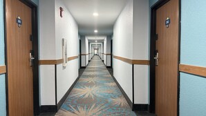 Un couloir d’hôtel avec des portes en bois, une moquette à motifs et une série de portes donnant sur les chambres.