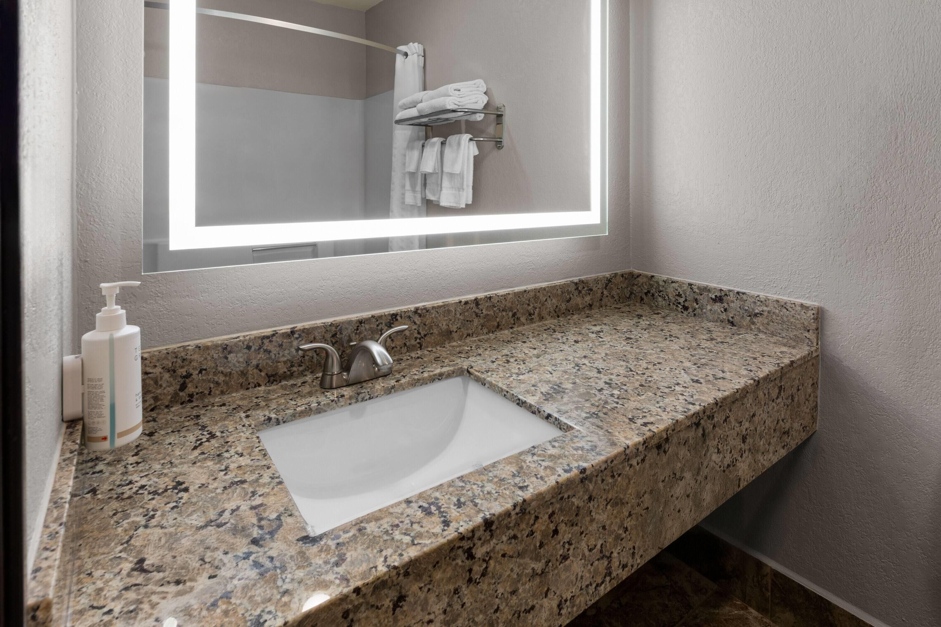 A bathroom with a granite countertop, a white sink, a faucet, and a mirror with a light.
