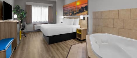 Ein Hotelzimmer mit Bett, Schreibtisch, Fernseher, einem Gemälde, einem Badezimmer mit Badewanne und einer Pflanze.