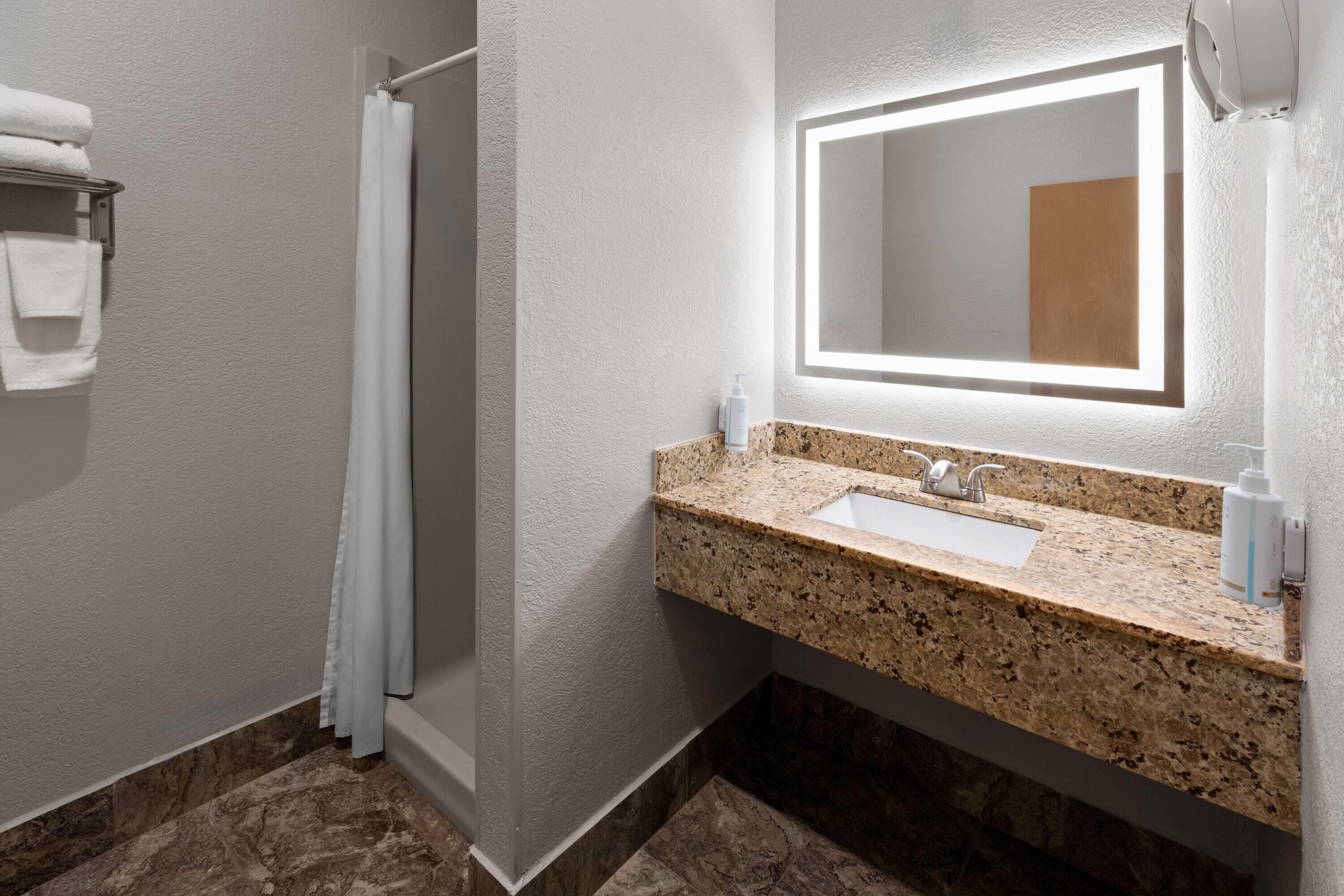 A bathroom with a granite countertop sink, a mirror, and a shower curtain.