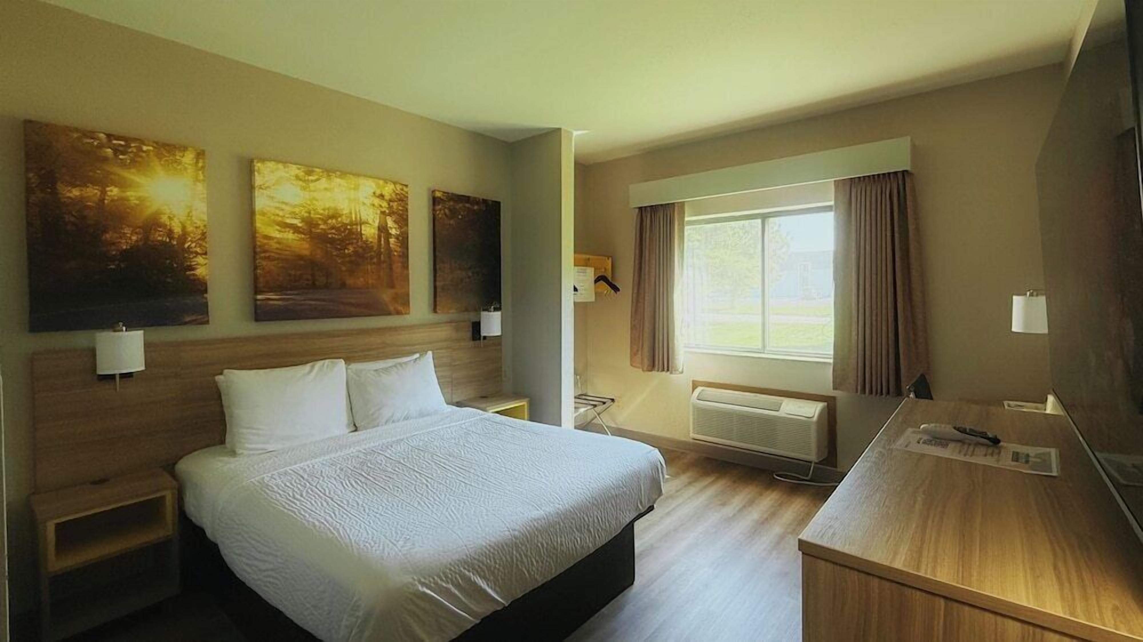 A hotel room with a bed, a desk, a TV, and three paintings on the wall.