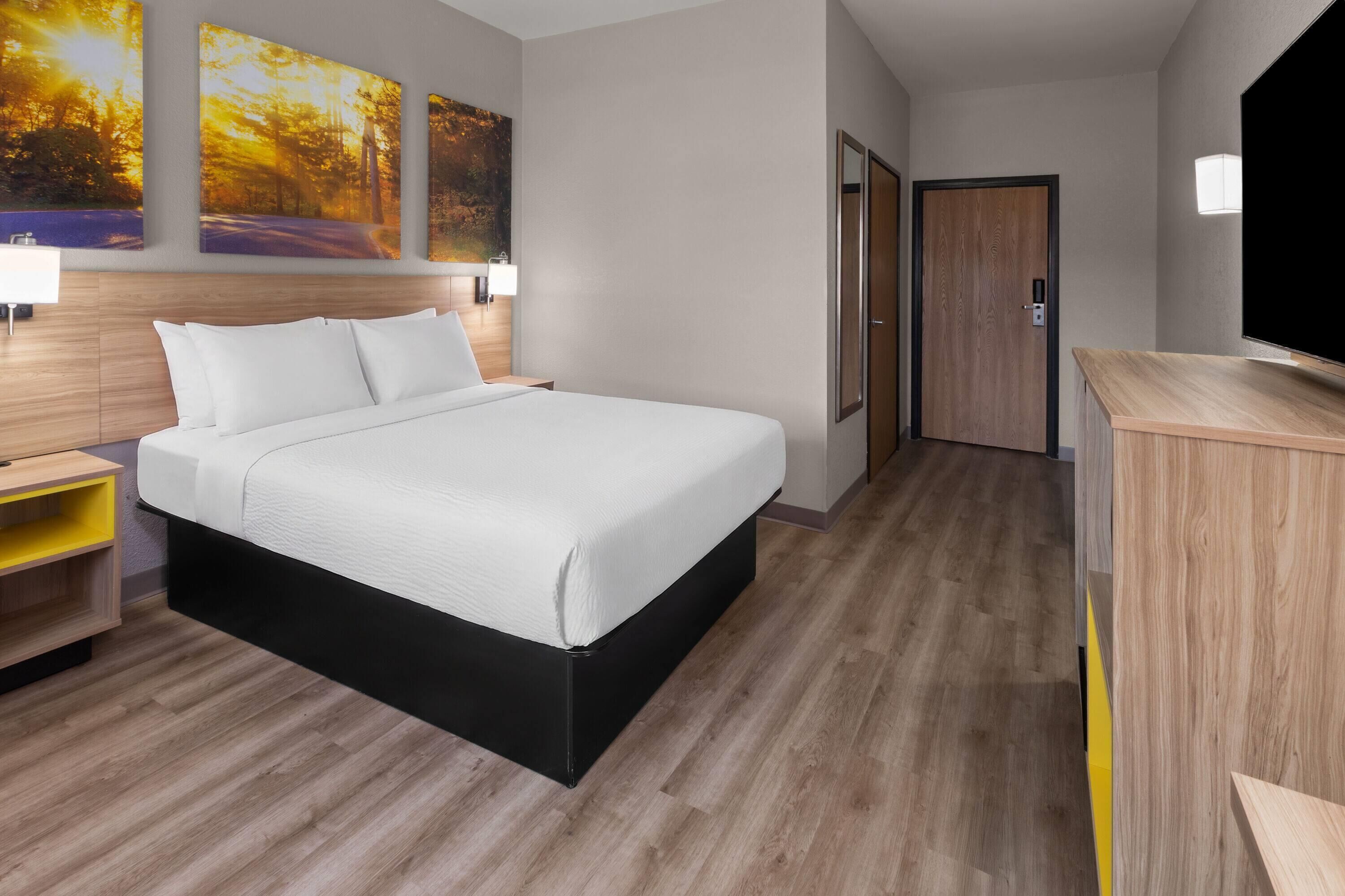 A hotel room with a bed, bedside tables, a TV, and artwork on the wall.
