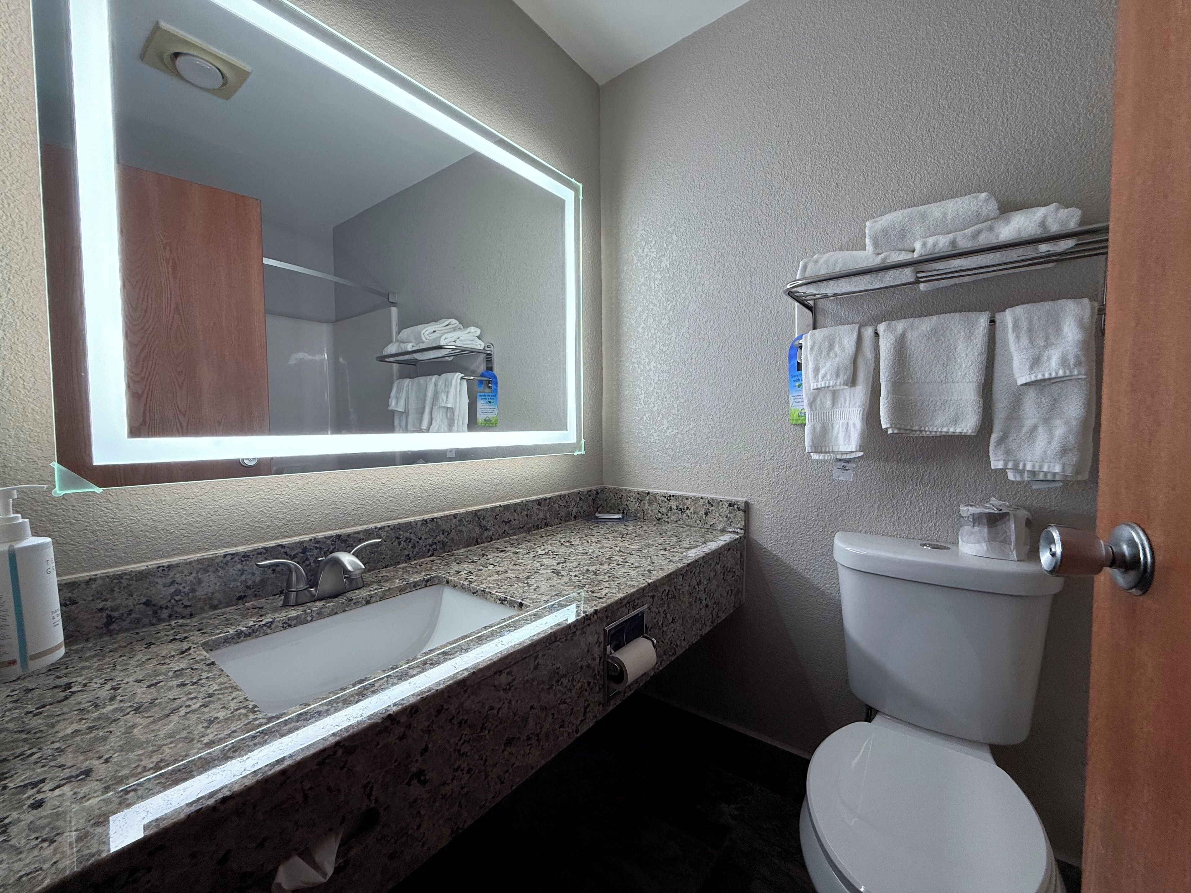 A bathroom with a granite countertop sink, a mirror, a toilet, and a towel rack with towels.