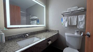 A bathroom with a granite countertop sink, a mirror, a toilet, and a towel rack with towels.