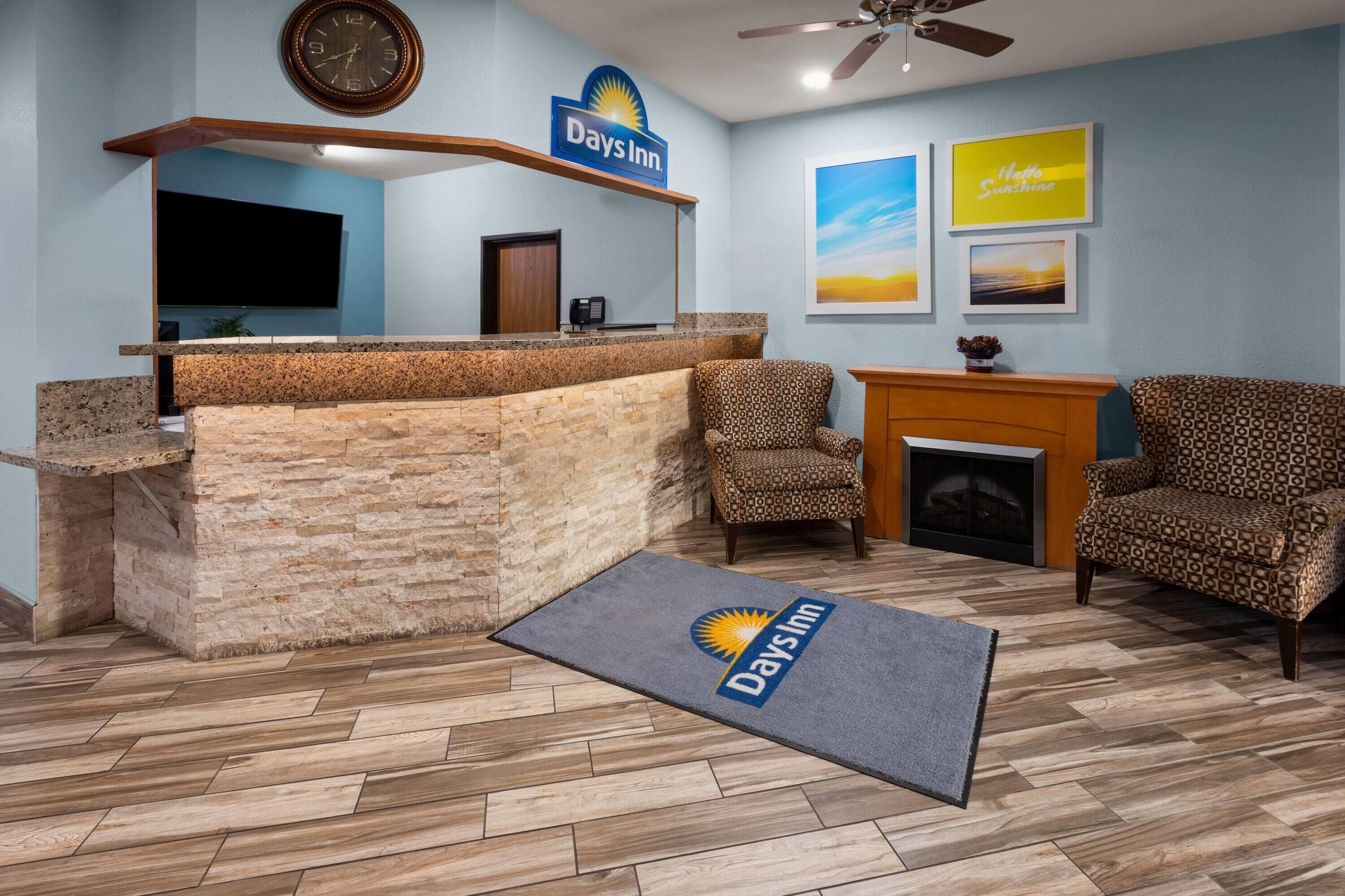 A reception area with a Days Inn sign, a fireplace, patterned chairs, and a doormat.