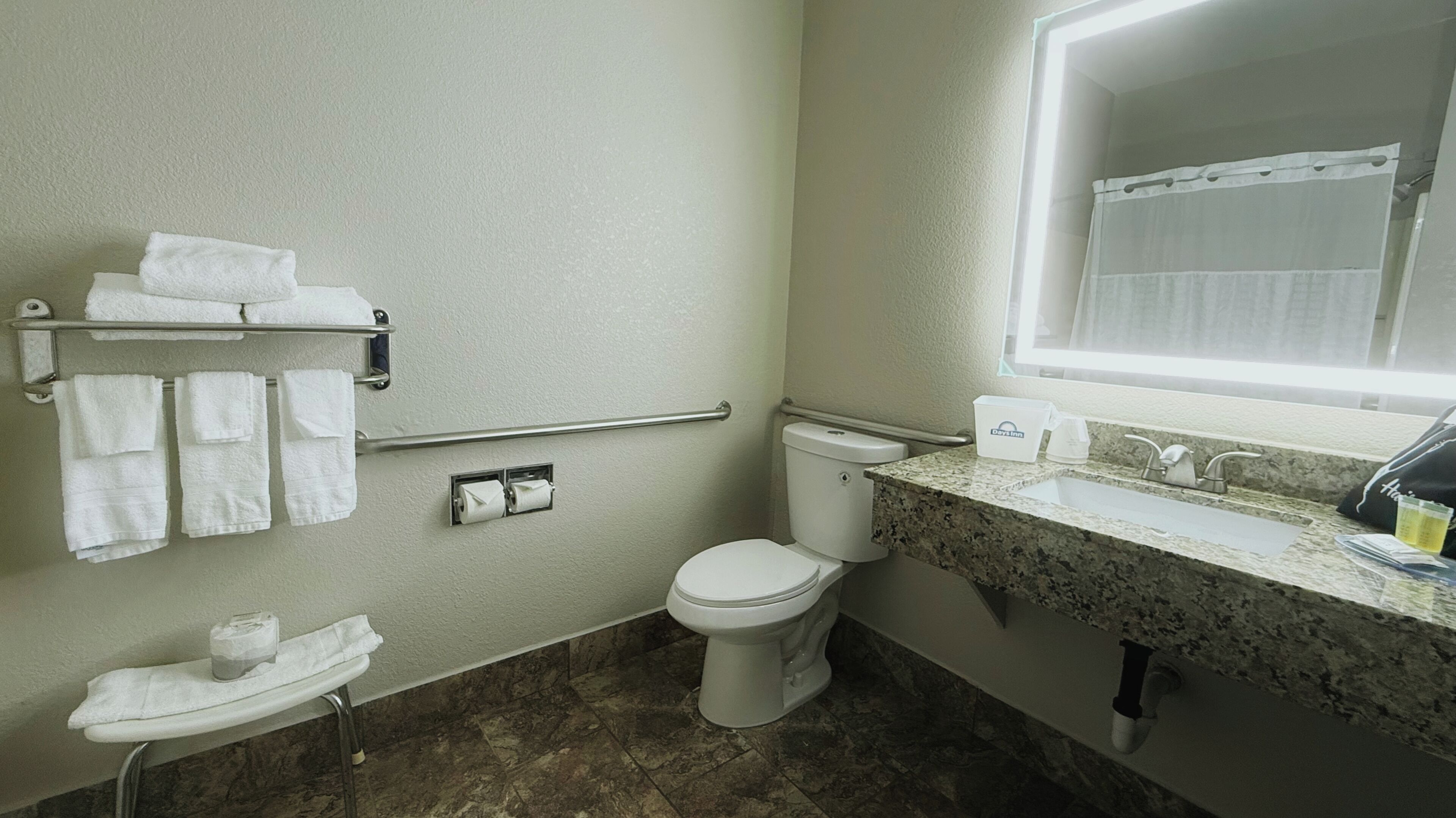 Un baño con inodoro, lavamanos, toallero y espejo.