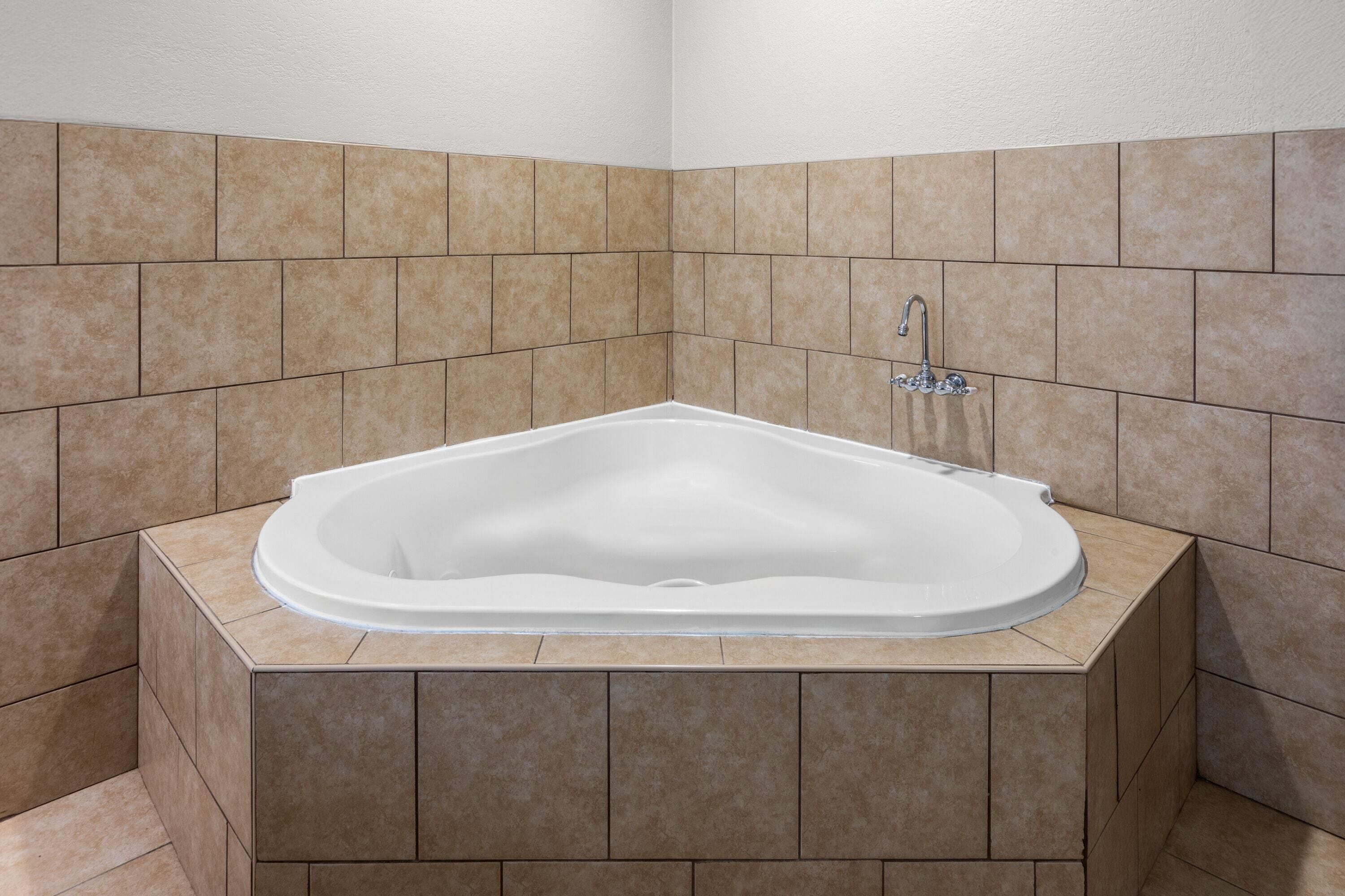 A corner bathroom with a freestanding bathtub, tiled walls, and a corner sink.