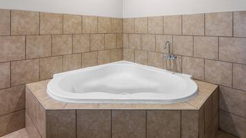 A corner bathroom with a freestanding bathtub, tiled walls, and a corner sink.