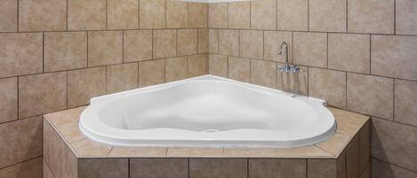 A corner bathroom with a freestanding bathtub, tiled walls, and a corner sink.