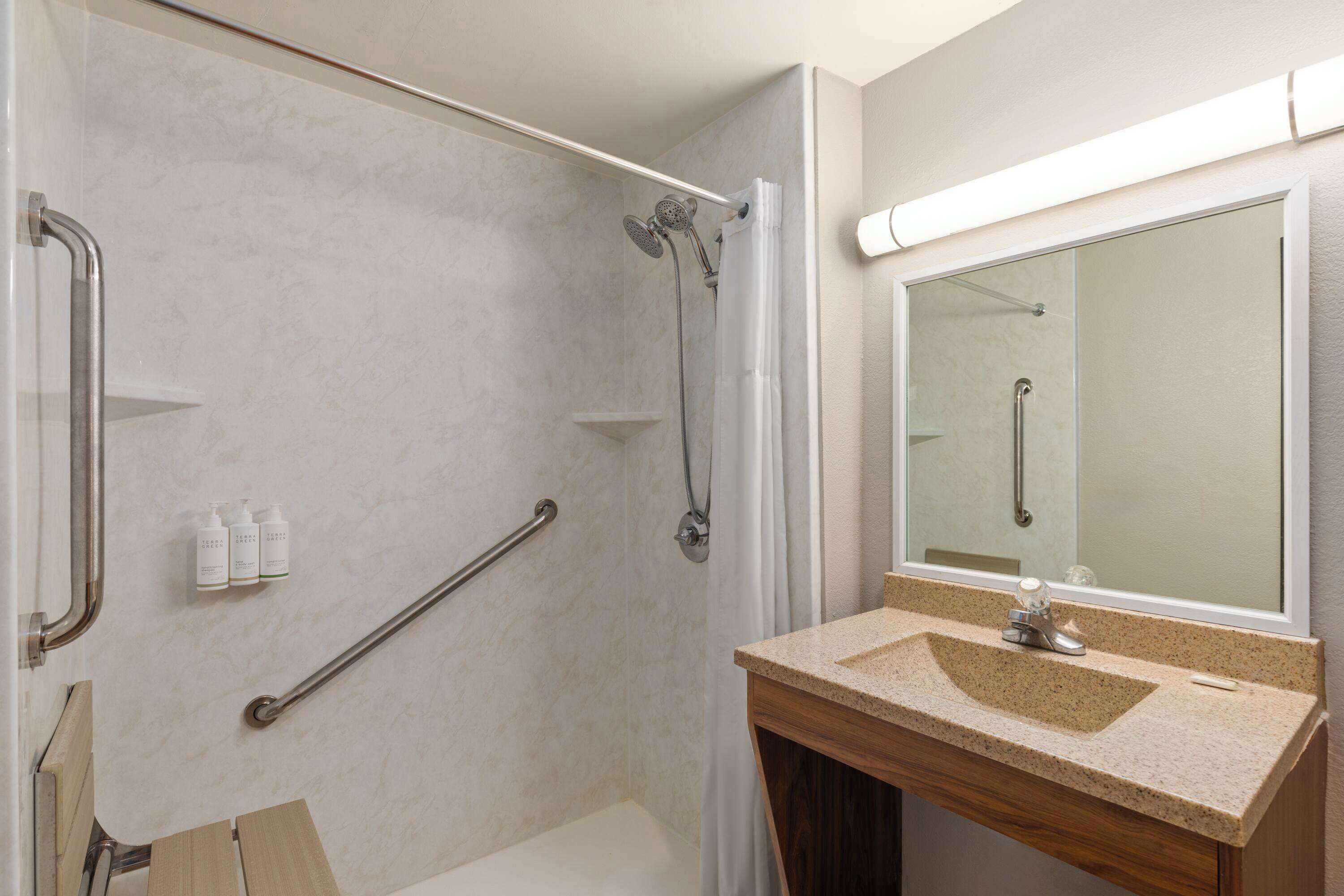 A bathroom with a shower, grab bars, a sink, and a mirror.