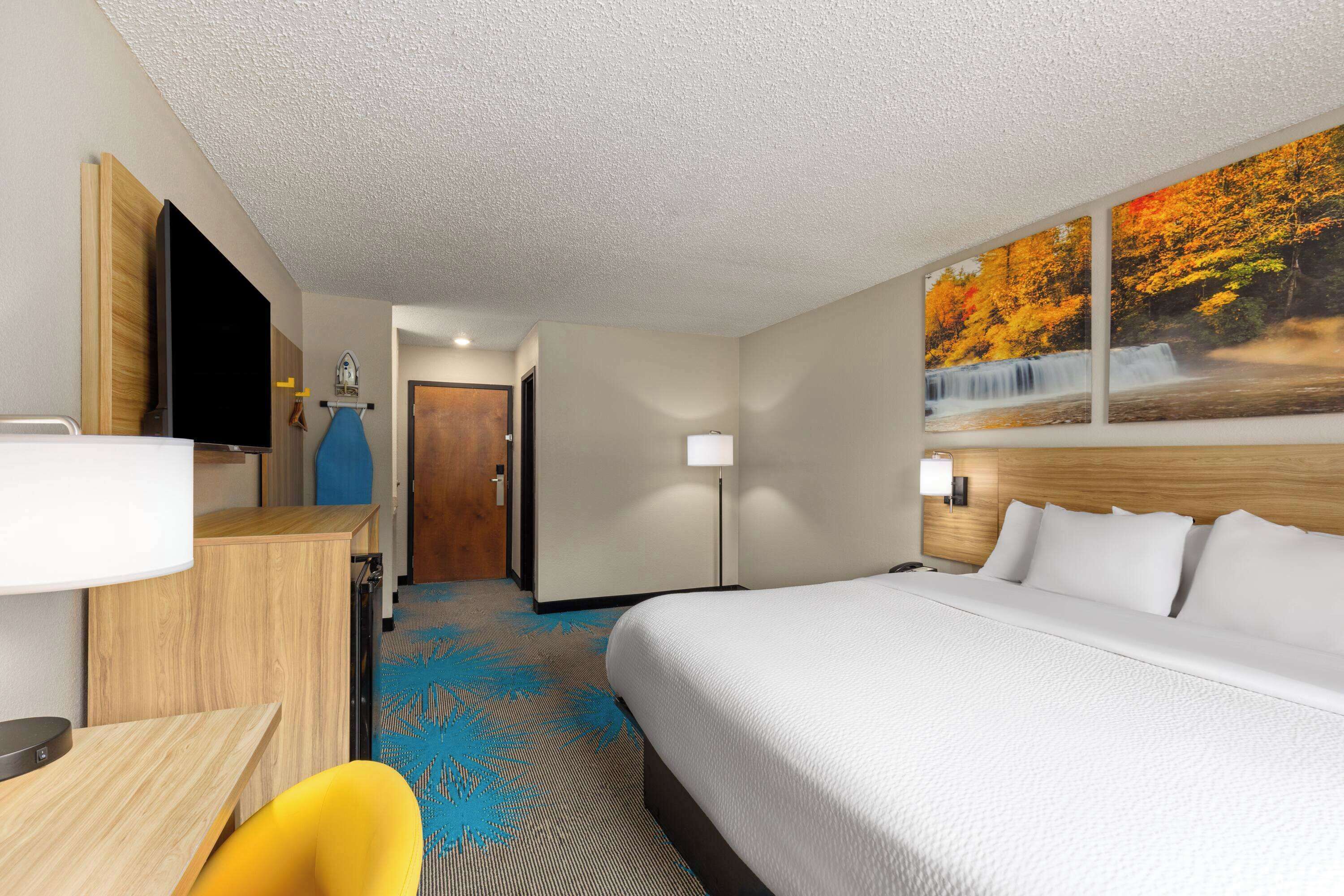 A hotel room with a bed, a desk, a chair, a TV, and a painting of a waterfall.