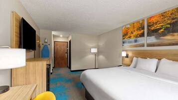 A hotel room with a bed, a desk, a chair, a TV, and a painting of a waterfall.