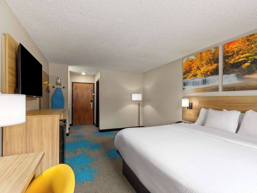 A hotel room with a bed, a desk, a chair, a TV, and a painting of a waterfall.