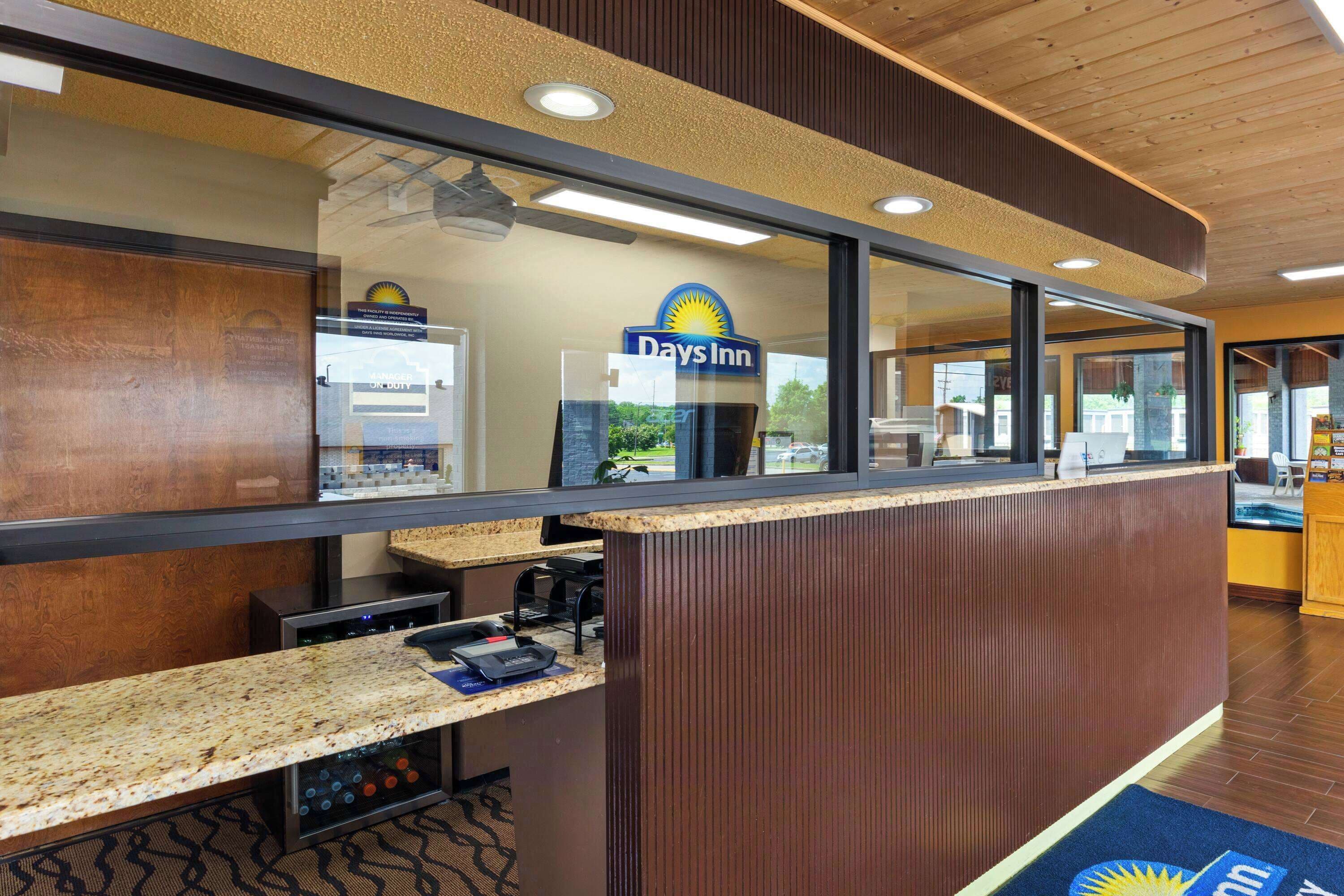 A reception area with a Days Inn sign, a counter with a computer and a phone, and a wooden floor.