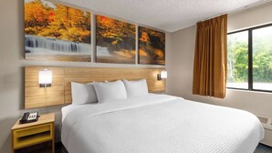 A hotel room with a large bed, a wooden headboard, a nightstand with a phone, and a window with curtains. - Days Inn by Wyndham Glasgow (Glasgow)