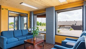 A modern interior with a blue sofa, wooden table, and large windows offering a view of the parking lot and buildings outside. - Days Inn by Wyndham Glasgow (Glasgow)