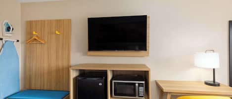 A compact hotel room with a bed, a desk with a chair, a microwave, a TV, and a small refrigerator.