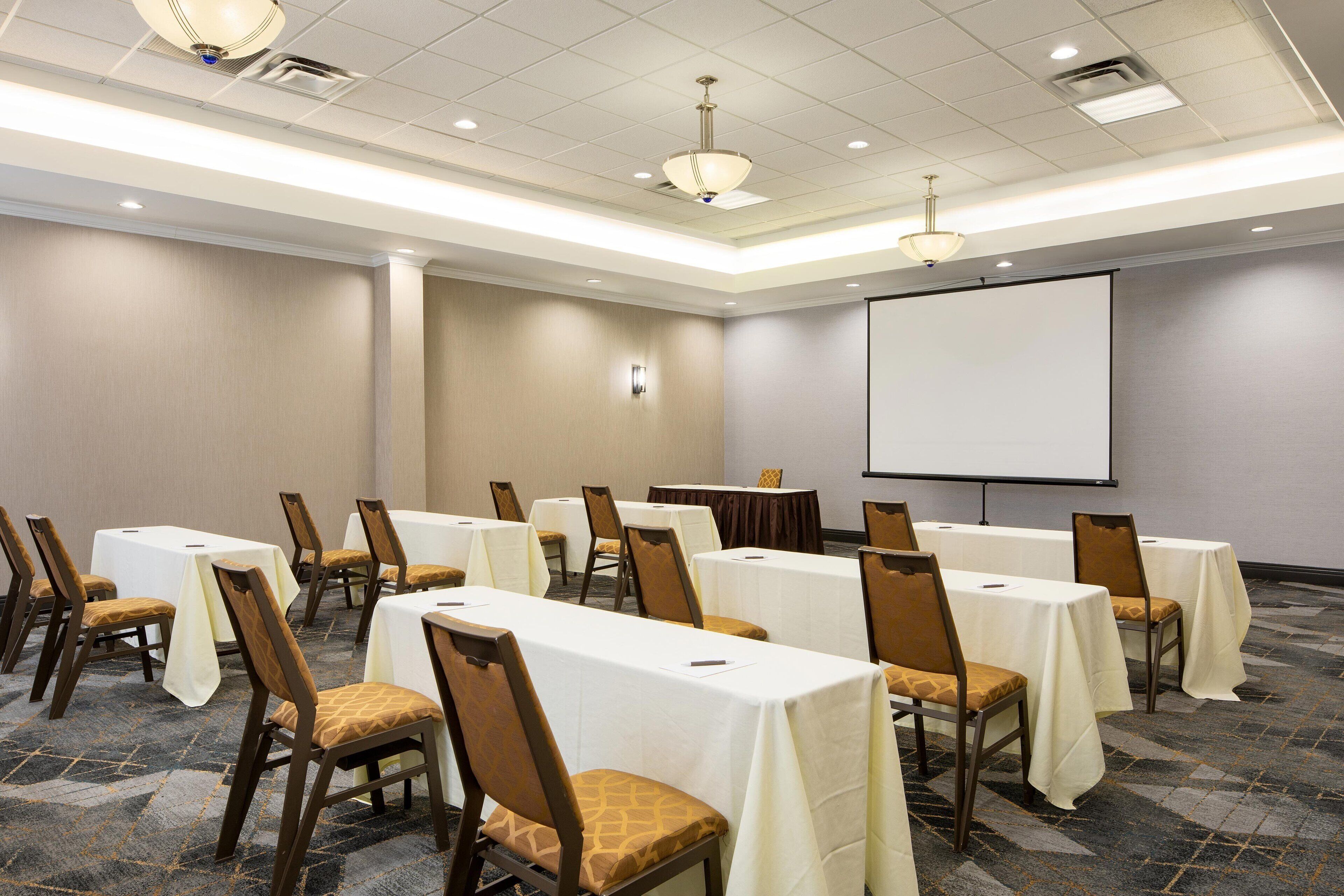 A conference room with tables and chairs, a projector screen, and a carpeted floor.